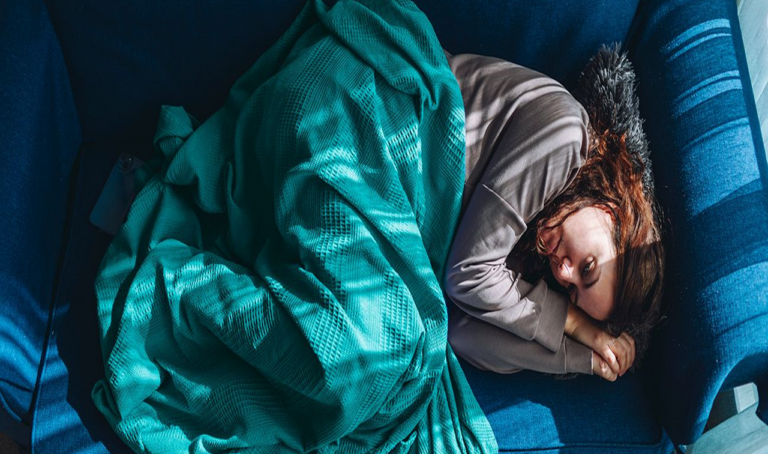 Une jeune femme dans la trentaine est allongée sur un sofa, manifestant des signes de dépression. Elle semble mélancolique et abattue.