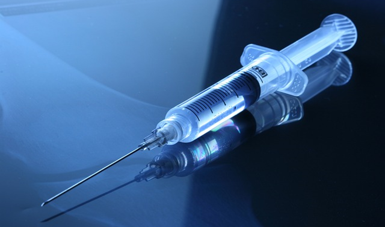 Une seringue de vaccin, remplie d'un liquide transparent, est posée sur une table.