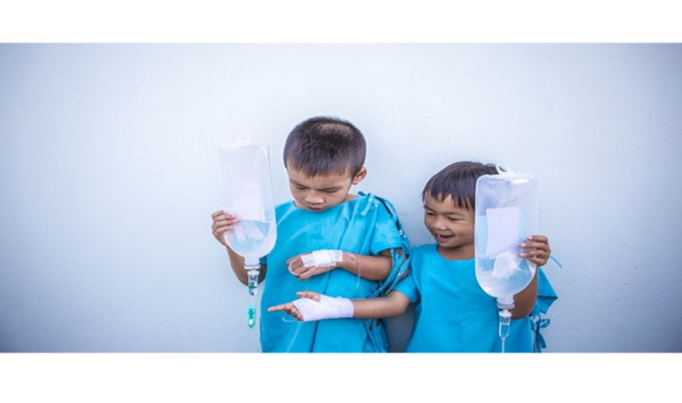 Deux enfants asiatiques en tenue hospitalière se tiennent debout côte à côte, chacun tenant un sac de perfusion intraveineuse dans ses mains.