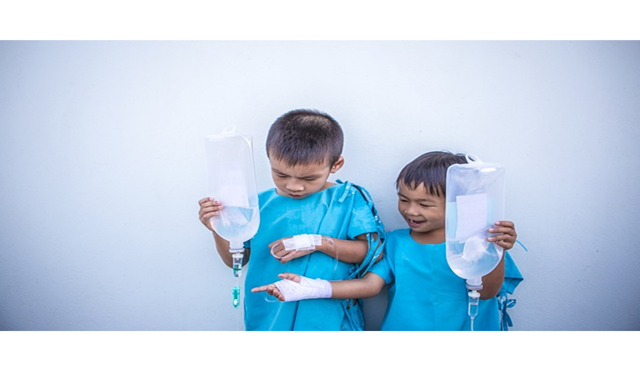 Deux enfants asiatiques en tenue hospitalière se tiennent debout côte à côte, chacun tenant un sac de perfusion intraveineuse dans ses mains.