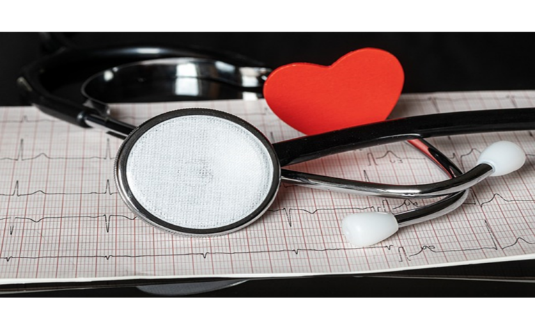 Un stéthoscope repose sur une feuille d’électrocardiogramme, avec un cœur rouge en papier placé entre ses oreillettes.