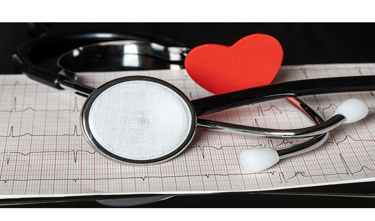 Un stéthoscope repose sur une feuille d’électrocardiogramme, avec un cœur rouge en papier placé entre ses oreillettes.