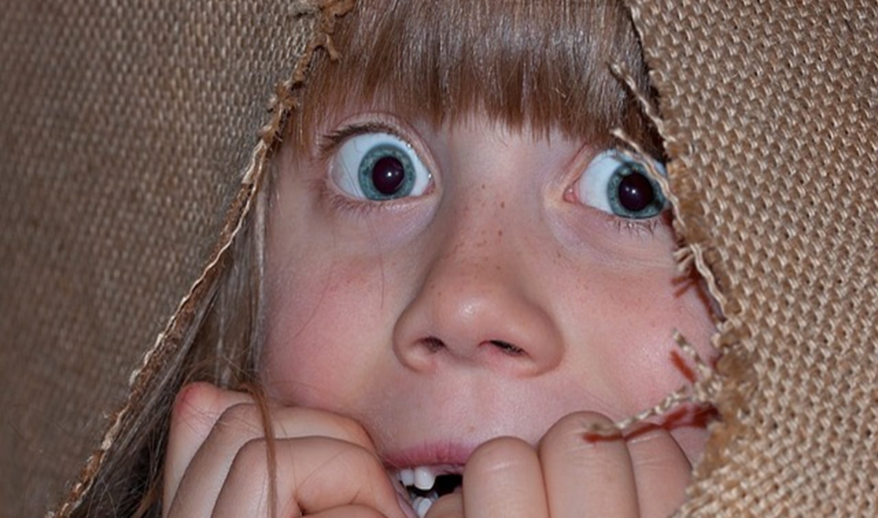 Une jeune fille d’environ 7 ans se ronge les ongles tout en fixant le lecteur avec une expression anxieuse.