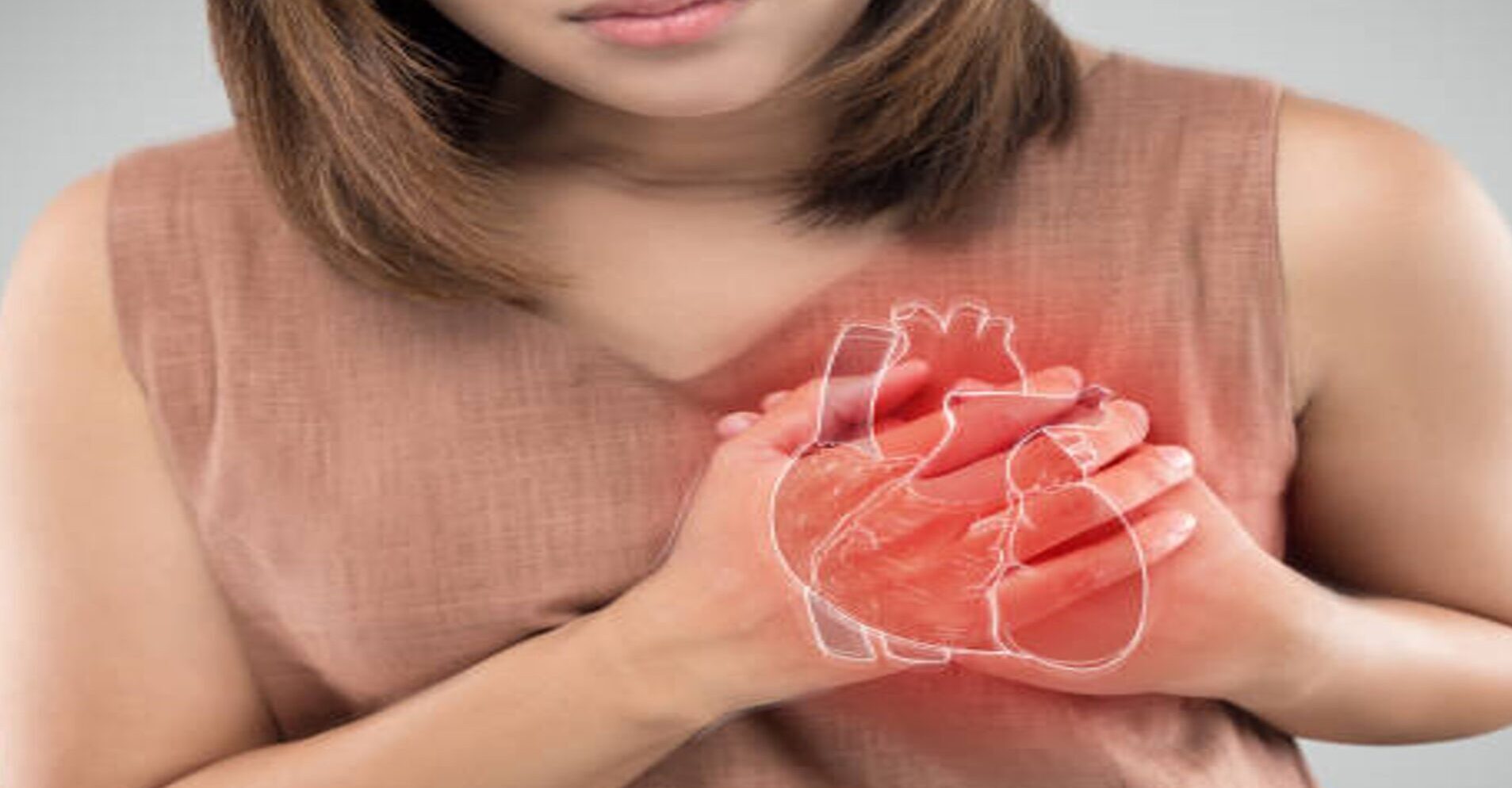 Une femme tient sa poitrine, plus précisément la partie gauche, avec ses deux mains, affichant une expression de douleur sur son visage. Un dessin de cœur, coloré en rouge, est superposé à l’endroit où ses mains sont posées.